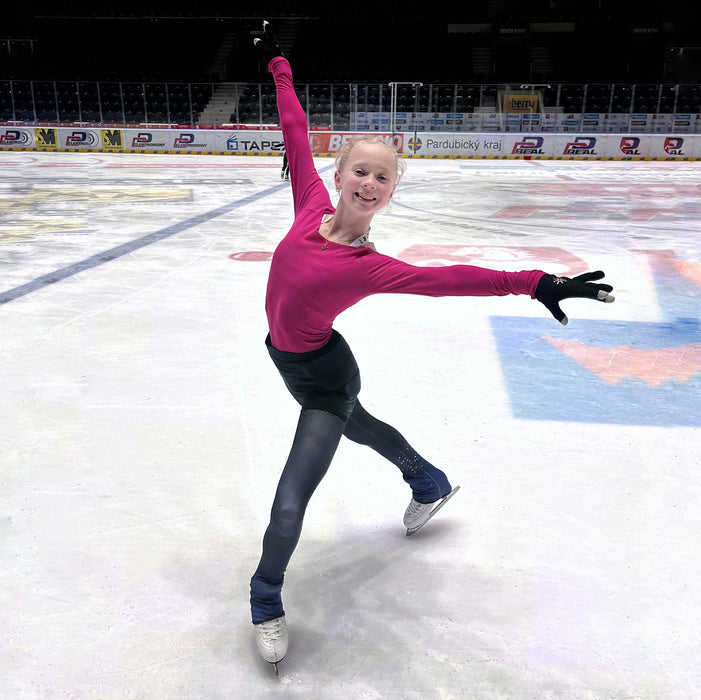 Person in a pink top and black pants skating on an ice rink.