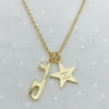 Gold necklace with a star charm and an ice skate blade charm, both charms are engraved, the heart with 'Believe In Yourself' . On a light gray background.