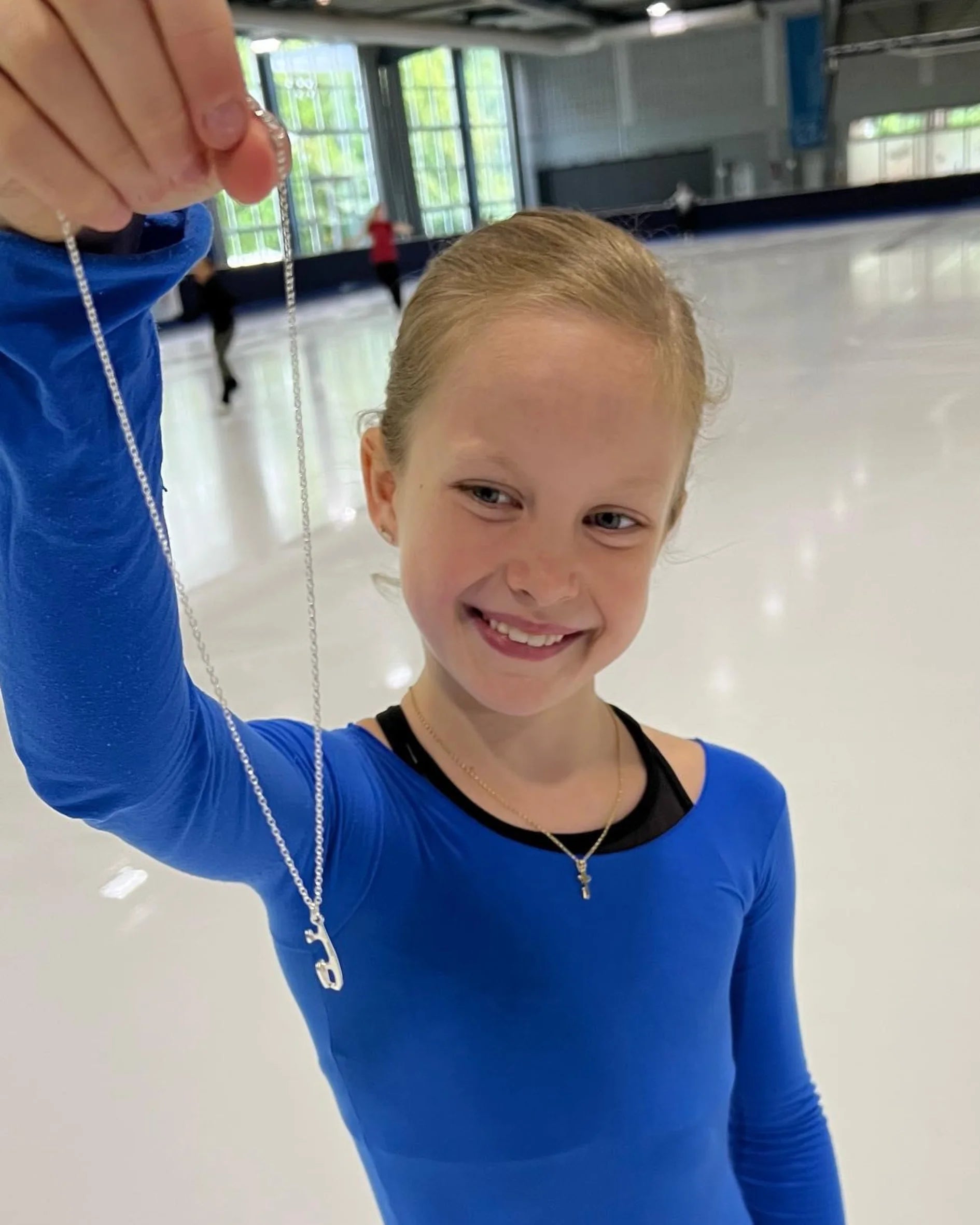 young female figure skater standing on ice holding a silver ice skating necklace
