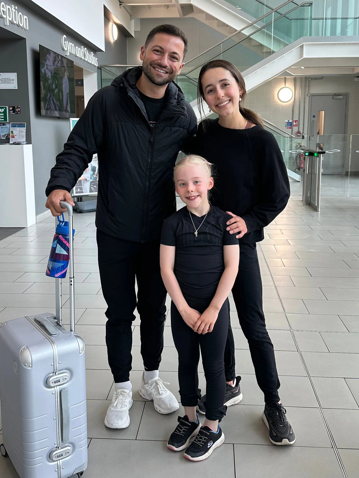 lilah fear and lewis gibson standing with a young female figure skater who is wearing a silver ice skating necklace