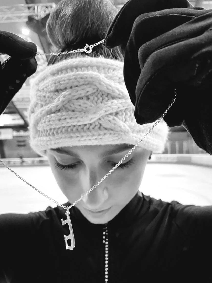 black and white image of a figure skater on ice holding a silver ice skating necklace up in front of her