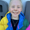 Child wearing a colorful jacket wearing a silver necklace with a snowflake and ice skate blade charm with a blurred background