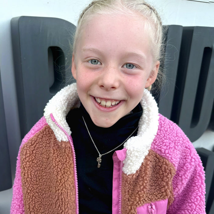 young smiling female figure skater wearing a pink and brown jacket and a silver necklace with a skate blade and snowflake char