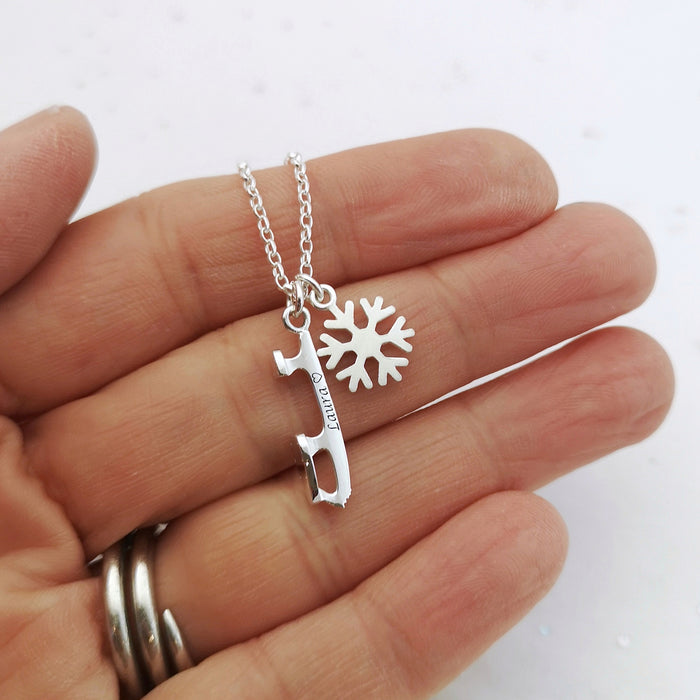 Personalised Silver Ice Skating Blade Necklace with a silver snowflake, bring held in a hand for scale. 