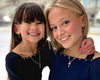 Close up of two figure skaters in dark blue and black tops on an ice rink wearing gold ice skate blade necklaces
