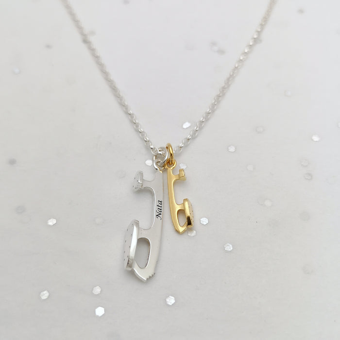 close up shot of a necklace featuring two tiny ice skate blades, one in silver and one in gold plated silver