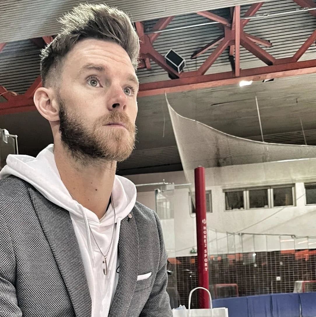 figure skater phil harris wearing a jacket white hoodie and grace and strength ice skating necklace