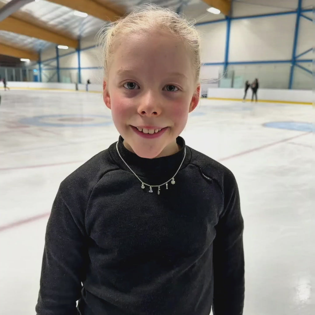 young figure skater on ice in a black top wearing a silver ice skating charm necklace