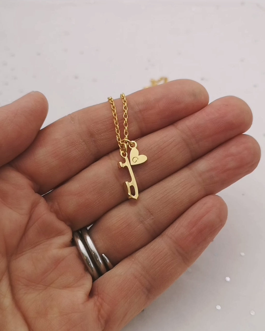 hand holding a gold necklace featuring a personalised heart and an ice skate blade charm