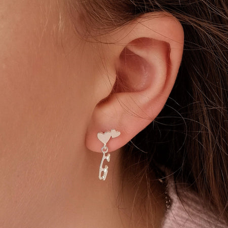 close up of a girl in a pink sweater wearing a silver earring which features an ice skate blade and two hearts