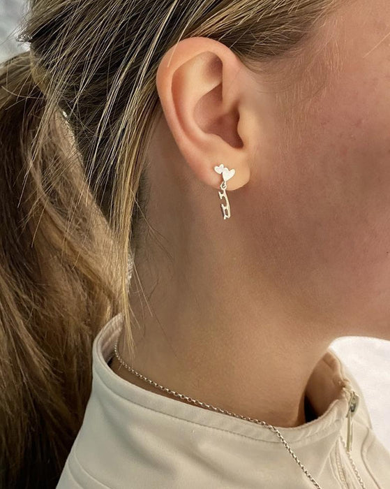 figure skater on ice wearing silver ice skate blade and heart stud earrings