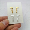 silver and gold love ice skate blade and hearts stud earrings being held in a hand on a white background