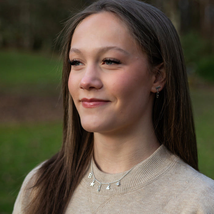 Woman with long brown hair wearing a beige sweater and necklace outdoors