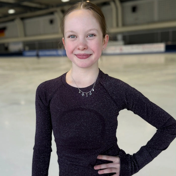 figure skater standing on ice in a dark top wearing a silver charm necklace with a star, heart, skate blade and an H