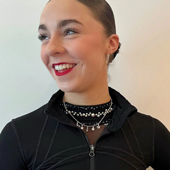 figure skater wearing a sparkly dress and a silver charm necklace with a black jacket