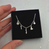 Silver necklace with charms in a black box held by a hand on a light gray background