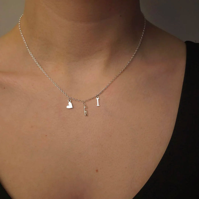 silver necklace with 3 charms, heart, ice skate blade and letter I, close up  on a model
