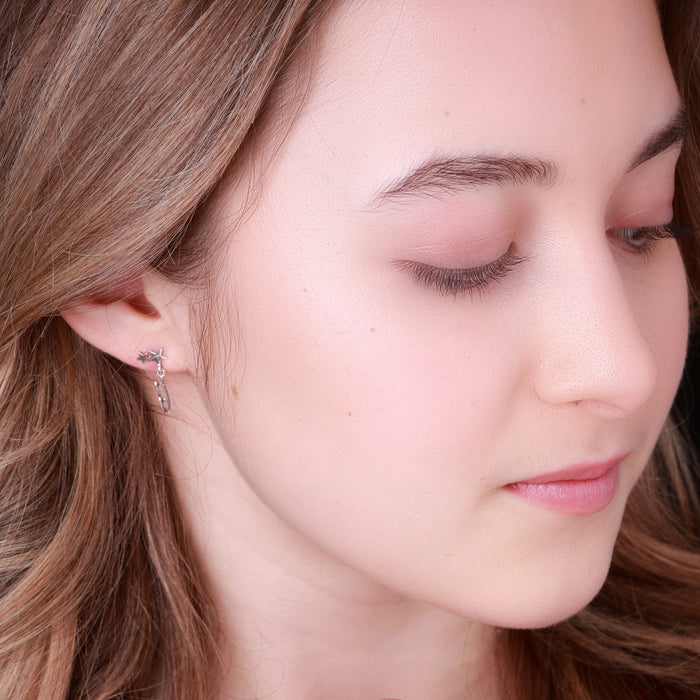 close up image of a figure skater wearing silver shine bright ice skating earrings which feature tiny skate blades and stars