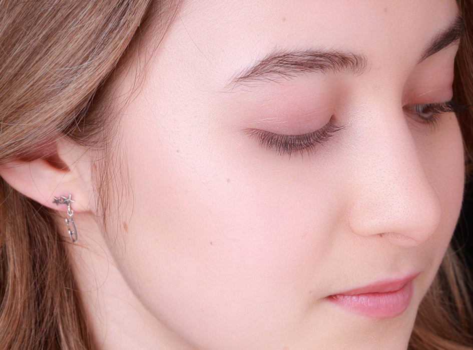 close up image of a figure skater wearing silver shine bright ice skating earrings which feature tiny skate blades and stars