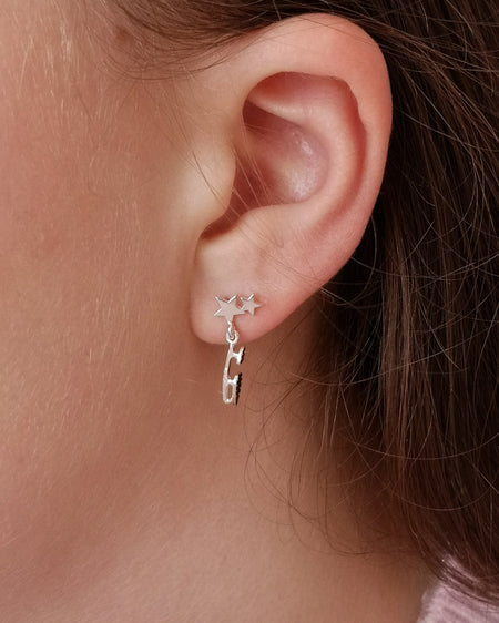 close up of a girl wearing silver earrings with an ice skate blade and stars