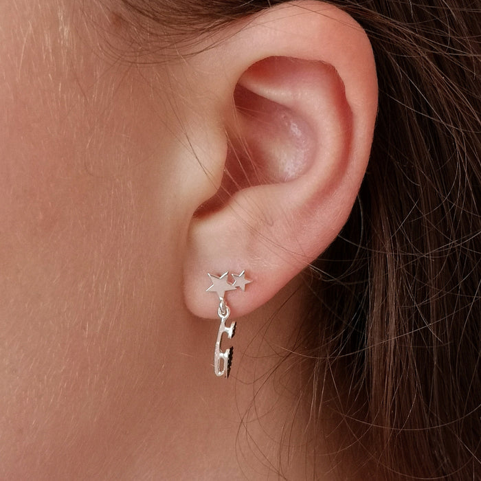 close up of a girl wearing silver earrings with an ice skate blade and stars