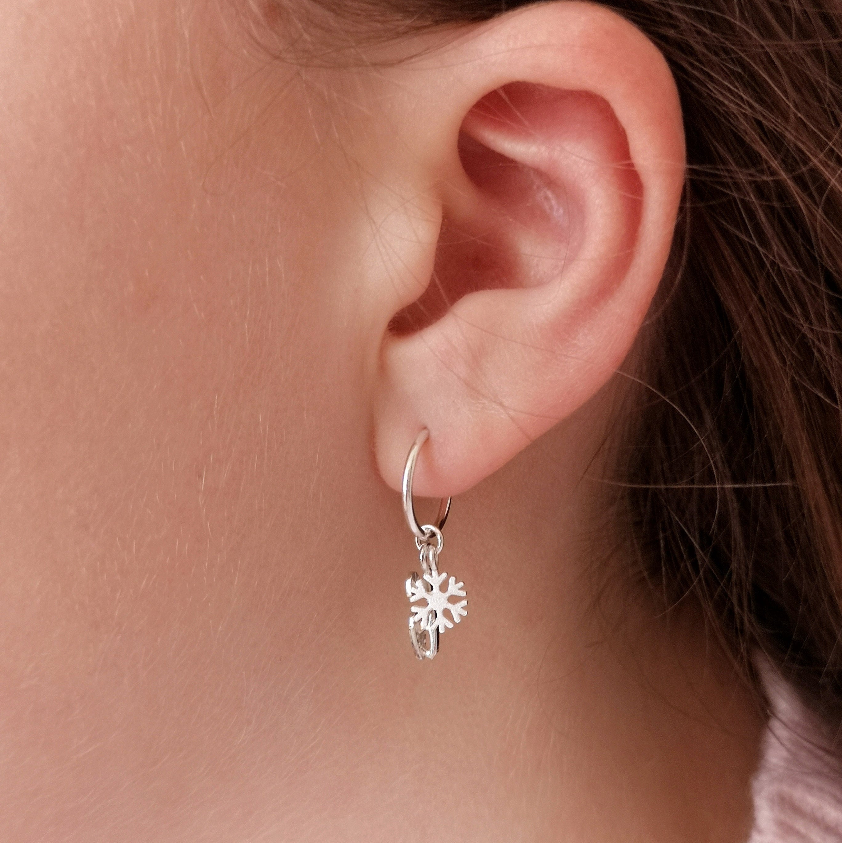 close up of a girl wearing a silver ice skate blade and snowflake hoop earring