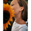 Woman holding a sunflower close to her face wearing silver ice skating hoop earrings
