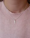 girl in a pink sweater wearing a silver necklace with an ice skate blade and a snowflake charm