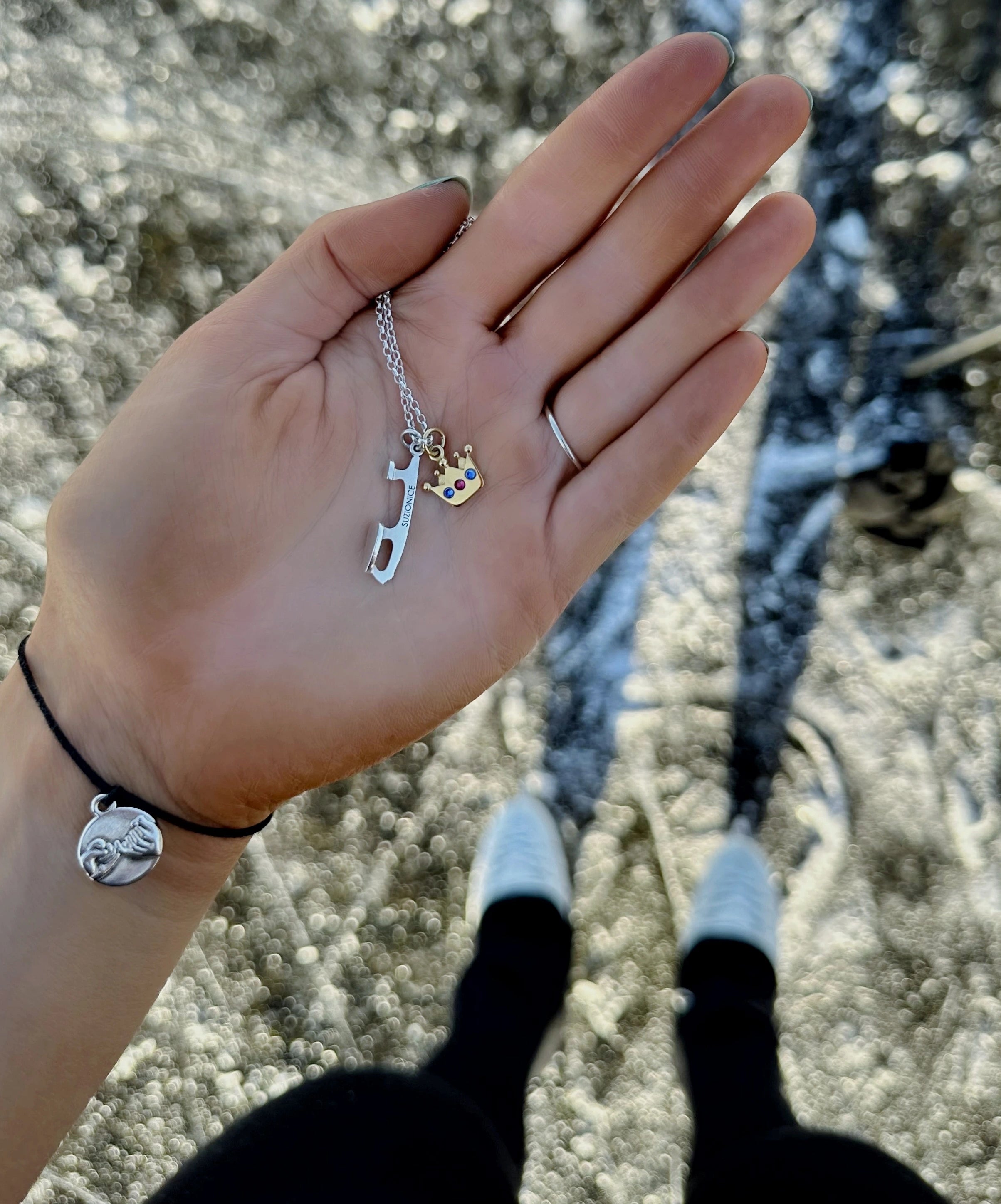 a figure skater standing on frozen ice holding a personalised silver ice skating necklace and a gold crown charm