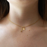 close up of a gold necklace featuring a star and an ice skate blade charm being worn